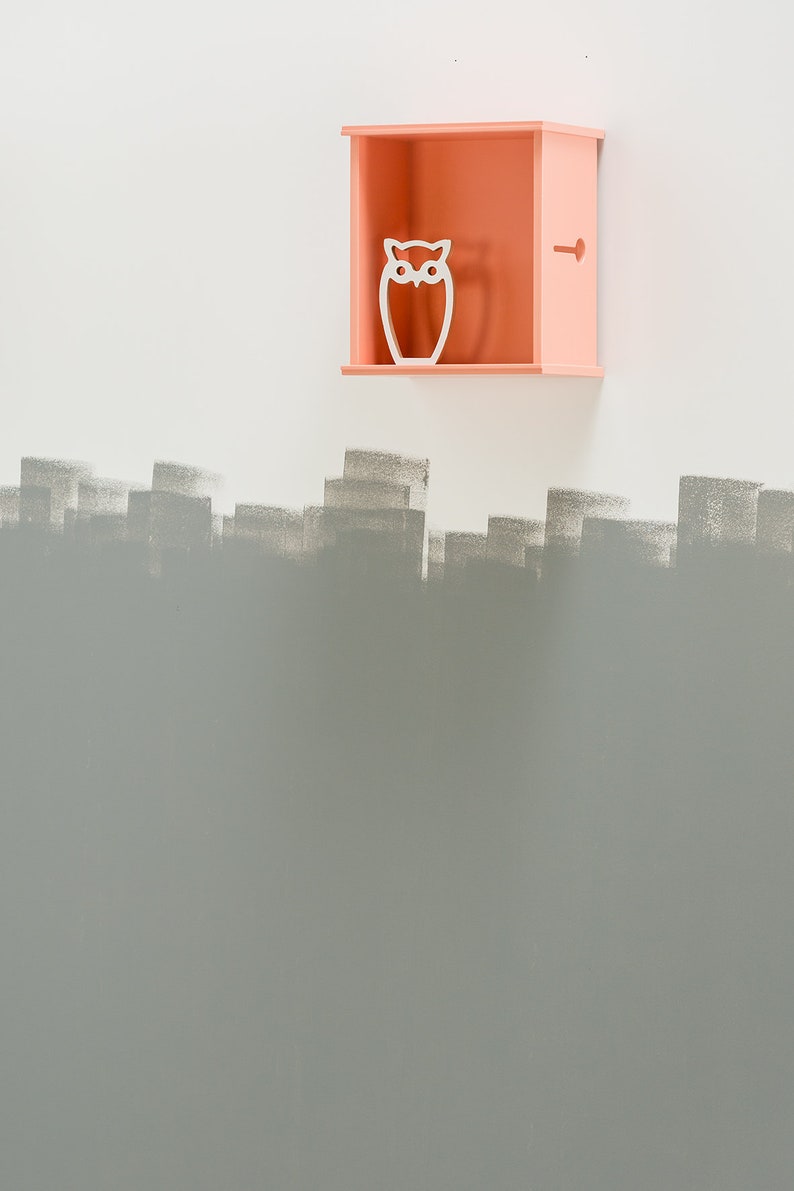 May include: A light pink wooden shelf with a white owl figurine inside. The shelf is mounted on a wall that is painted half white and half grey.