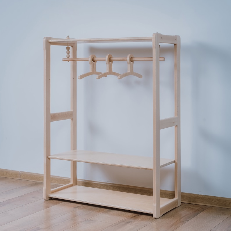 May include: A wooden clothes rack with a shelf and a hanging bar. The rack is made of natural wood and has a simple design.