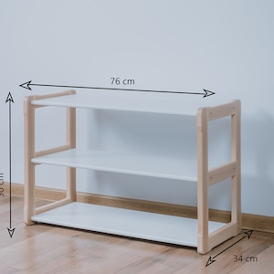 May include: White wooden shelf unit with three shelves. The shelf is 76 cm wide, 50 cm tall, and 34 cm deep.
