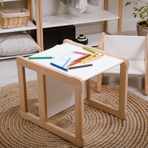 Pode incluir: Uma mesa de madeira branca com uma superfície branca e um conjunto de lápis de cor sobre ela. A mesa está sobre um tapete marrom com uma cadeira branca ao lado.