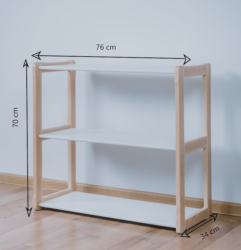 May include: White shelf unit with three shelves and a natural wood frame. The shelf unit is 76 cm wide, 70 cm tall, and 34 cm deep.