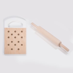 Puede incluir: Un rodillo de madera y una tabla de cortar de madera con agujeros. La tabla de cortar tiene una parte superior blanca y una parte inferior de madera natural.