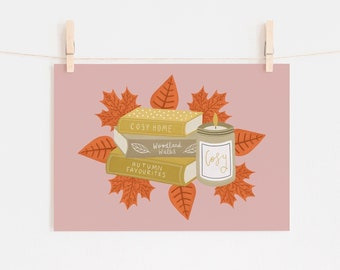 May include: A print featuring a stack of books with titles "Cosy Home", "Woodland Walks", and "Autumn Favourites", a lit candle, and autumn leaves. The candle has the word "Cosy" on it. The background is a light pink.