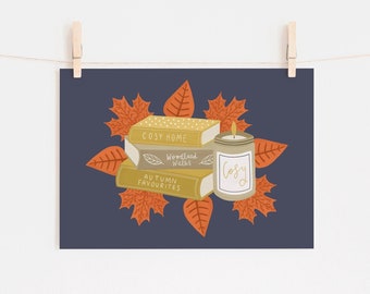 May include: A print featuring a stack of books with the titles "Cosy Home", "Woodland Walks", and "Autumn Favourites". A lit candle and orange leaves surround the books. The word "Cosy" is written on the candle. The background is a dark blue.