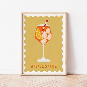 Peut inclure: Une illustration jaune et orange d'un cocktail Aperol Spritz dans un verre &agrave; pied avec une paille rouge et blanche. Le texte "APEROL SPRITZ" est sous le verre.