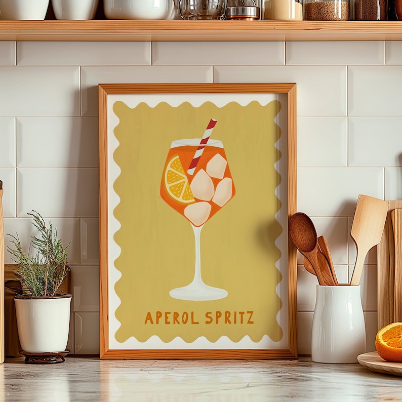 Peut inclure: Une impression encadr&eacute;e avec un fond jaune et une bordure blanche festonn&eacute;e. L'impression pr&eacute;sente une illustration d'un cocktail Aperol Spritz avec une paille rouge et blanche, une tranche d'orange et des gla&ccedil;ons. Le texte "Aperol Spritz" est imprim&eacute; en noir en bas de l'impression.