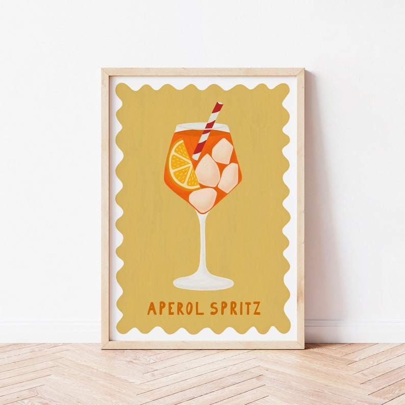 Peut inclure: Une illustration jaune et orange d'un cocktail Aperol Spritz dans un verre &agrave; pied avec une paille rouge et blanche. Le texte "APEROL SPRITZ" est sous le verre.