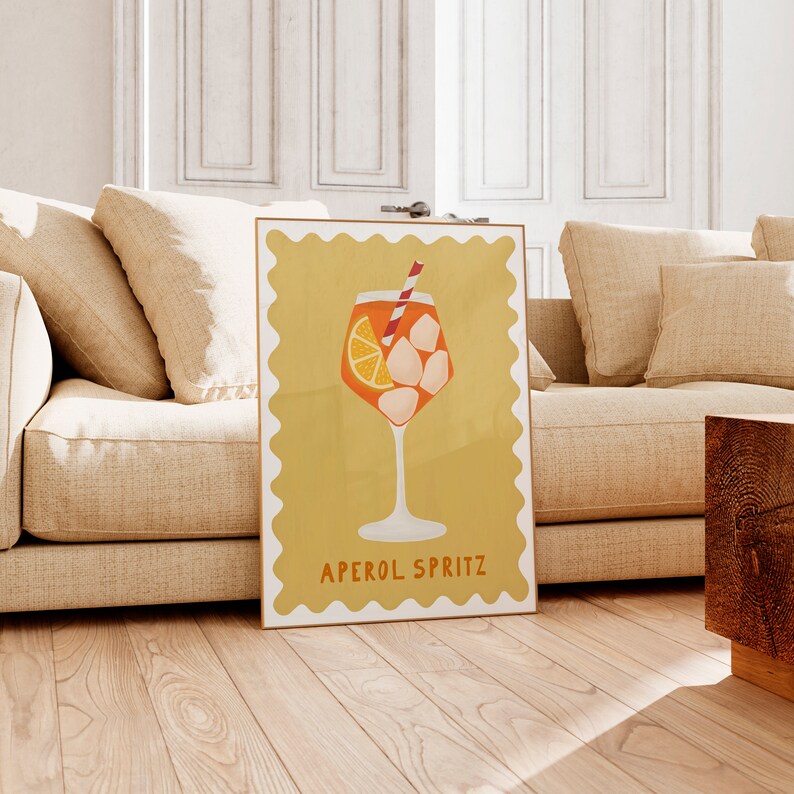 Peut inclure: Une affiche jaune avec une bordure blanche et un bord festonn&eacute;. L'affiche repr&eacute;sente un verre d'Aperol Spritz avec une tranche d'orange, des gla&ccedil;ons et une paille rouge et blanche. Le texte "APEROL SPRITZ" est imprim&eacute; en noir en bas de l'affiche.