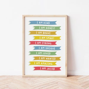 K&ouml;nnte beinhalten: Ein gerahmter Druck mit wei&szlig;em Hintergrund und bunten Bannern mit positiven Affirmationen. Der Text auf den Bannern lautet: "Ich bin freundlich", "Ich bin ehrlich", "Ich bin mutig", "Ich bin klug", "Ich bin stark", "Ich bin einzigartig", "Ich bin geliebt", "Ich bin gewollt", "Ich bin gro&szlig;artig", und "Ich bin Jacob".