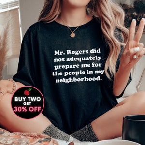 Puede incluir: Una camiseta negra con texto blanco que dice "Mr. Rogers did not adequately prepare me for the people in my neighborhood." Un gr&aacute;fico de cereza roja con el texto "BUY TWO GET 30% OFF" est&aacute; en la esquina inferior izquierda de la imagen.