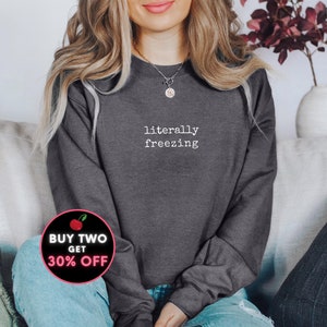 May include: Dark gray sweatshirt with the words "literally freezing" in white. A circular graphic with text that reads "BUY TWO GET 30% OFF" is in the lower left corner. The sweatshirt is a crew neck style.