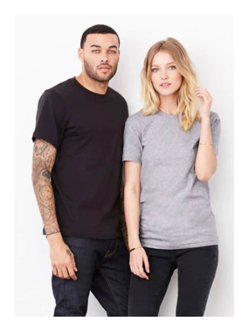 Peut inclure: Deux personnes portant des t-shirts, l'un noir et l'autre gris, se tenant l'un &agrave; c&ocirc;t&eacute; de l'autre. La personne &agrave; gauche porte un jean bleu et la personne &agrave; droite porte un pantalon noir.
