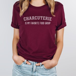Peut inclure: Un t-shirt bordeaux avec un texte blanc qui dit "CHARCUTERIE IS MY FAVORITE FOOD GROUP".