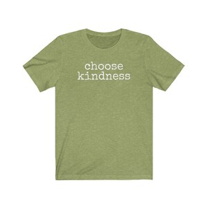 May include: A short-sleeved, olive green t-shirt with the words "choose kindness" printed in white block letters across the chest. The shirt has a crew neck and a casual, relaxed fit, suitable for everyday wear.