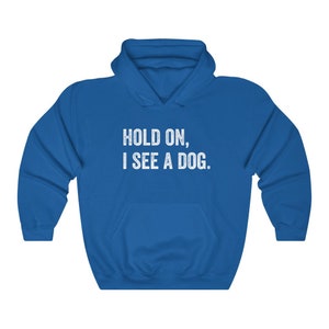 Pode incluir: Uma camisa de frio com capuz azul royal com o texto "HOLD ON, I SEE A DOG." impresso em branco.
