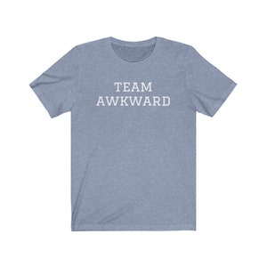 May include: A light blue t-shirt with the text "TEAM AWKWARD" printed in white on the front.