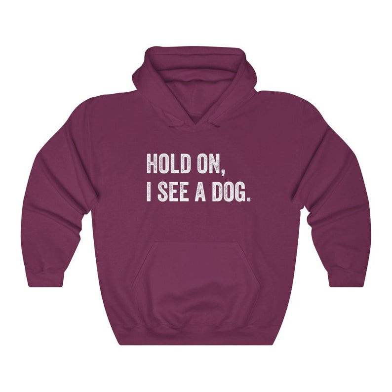 Pode incluir: Uma camisola de capuz cor vinho com o texto "HOLD ON, I SEE A DOG." impresso a branco na frente.