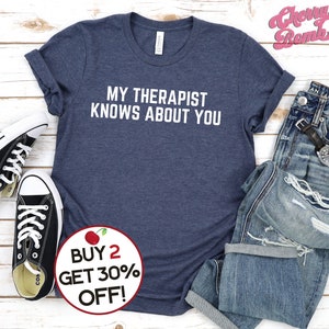 May include: A navy blue t-shirt with white text that reads "MY THERAPIST KNOWS ABOUT YOU". A red cherry graphic is in the lower right corner with the text "BUY 2 GET 30% OFF!"