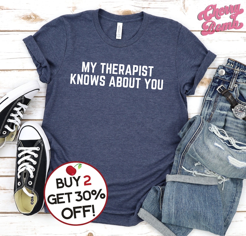 May include: A navy blue t-shirt with white text that reads "MY THERAPIST KNOWS ABOUT YOU". A red cherry graphic is in the lower right corner with the text "BUY 2 GET 30% OFF!"