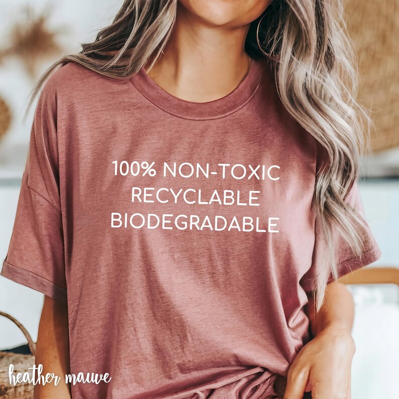 May include: Heather mauve t-shirt with the text "100% NON-TOXIC RECYCLABLE BIODEGRADABLE" in white. The shirt has a crew neck and short sleeves. The words "heather mauve" are written in cursive at the bottom left.