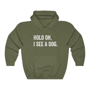 Pode incluir: Uma camisa de frio com capuz verde com o texto "HOLD ON, I SEE A DOG." impresso em branco na frente.