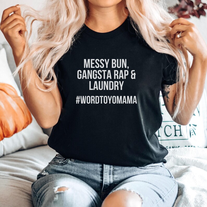 K&ouml;nnte beinhalten: Schwarzes T-Shirt mit wei&szlig;em Text: "Messy Bun, Gangsta Rap & Laundry" und dem Hashtag "#wordtoyomama". Das Shirt besteht aus einem weichen Material und eignet sich f&uuml;r Freizeitkleidung.