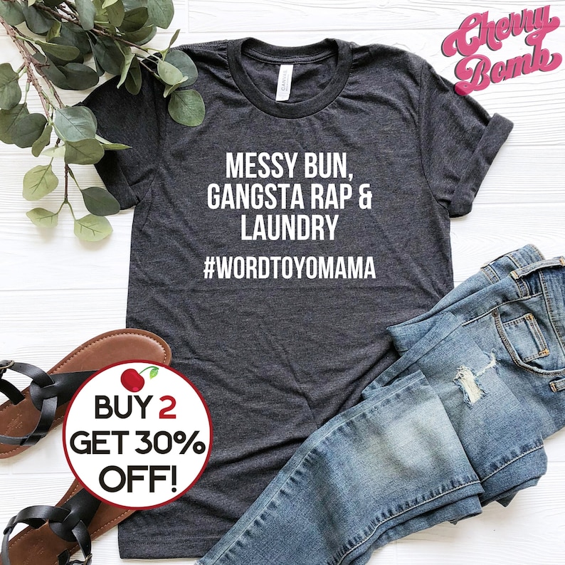 K&ouml;nnte beinhalten: Dunkelgraues T-Shirt mit dem wei&szlig;en Text "MESSY BUN, GANGSTA RAP & LAUNDRY #WORDTOYOMAMA". Das Shirt wird mit blauen Jeans und schwarzen Sandalen pr&auml;sentiert. Ein Aufkleber zeigt "BUY 2 GET 30% OFF!"