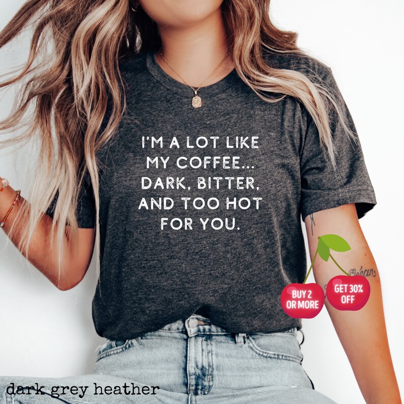 May include: Dark grey heather t-shirt with white text that reads "I'm a lot like my coffee... dark, bitter, and too hot for you."  The shirt is being modeled by a person wearing blue jeans. There are two red cherries on the person's arm with white text that reads "Buy 2 or more" and "Get 30% off".
