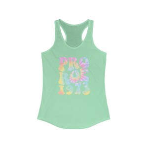 May include: A light green racerback tank top with the words "PRO ROE 1973" in a tie-dye design. The text is in shades of pink, yellow, and blue. The tank top has a scoop neck and a racerback design.