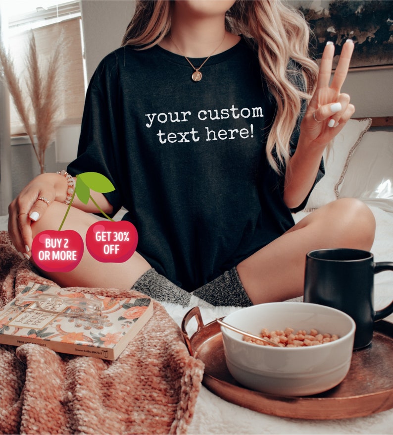 May include: Black t-shirt with the text "your custom text here!" in white. The image also includes a bowl of cereal, a black mug, and a copper tray. Two cherry graphics with text are also visible.