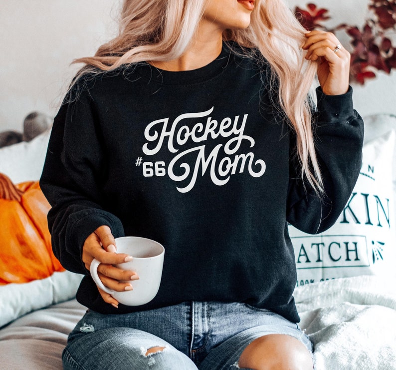 Może przedstawiać: Czarna bluza z napisem "Hockey #66 Mom" w białym, ozdobnym pismem.
