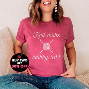 May include: A pink t-shirt with the text "Knit more worry less" in white. The text is accompanied by a graphic of a ball of yarn with knitting needles. A red circle with a white cherry and the text "BUY TWO GET 30% OFF" is in the lower left corner of the image.