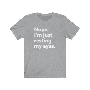 May include: A heather grey t-shirt with the text "Nope. I'm just resting my eyes." printed in white.