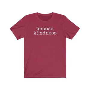 May include: A maroon t-shirt with the words "choose kindness" printed in white. The short-sleeved shirt is made of a soft material and is suitable for casual wear. The text is centered on the front of the shirt.