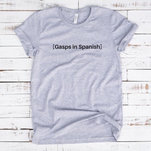 Peut inclure: T-shirt gris avec le texte "[Gasps in Spanish]" imprim&eacute; sur le devant.