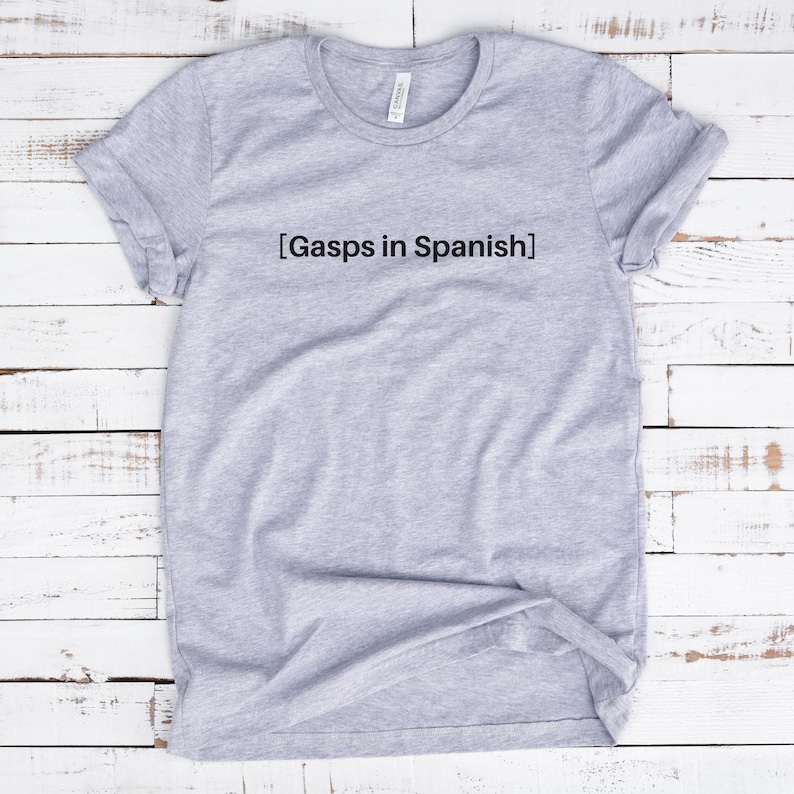 Peut inclure: T-shirt gris avec le texte "[Gasps in Spanish]" imprim&eacute; sur le devant.