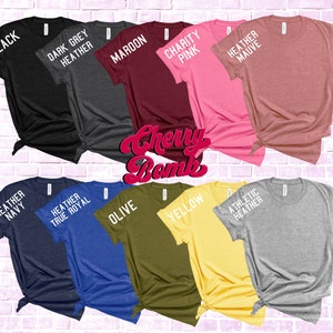 May include: A collection of ten t-shirts in various colors, including black, dark grey heather, maroon, charity pink, heather mauve, heather navy, heather true royal, olive, yellow, and athletic heather. Each shirt has a different color and a text label on the sleeve.