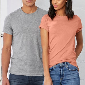 Peut inclure: Deux personnes portant des t-shirts &agrave; manches courtes. La personne &agrave; gauche porte un t-shirt gris chin&eacute; et la personne &agrave; droite porte un t-shirt corail. Les deux personnes portent un jean bleu.