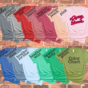 May include: A collection of various colored t-shirts, including heather gray, red, pink, and green. One shirt features the text "Cherry Bomb" in a retro font. Another shirt displays a "Color Chart" label. The shirts are displayed against a brick wall.