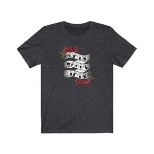 May include: A dark heather grey t-shirt featuring a white banner design that reads "Cats and Tats" with two red roses on either side of the banner.