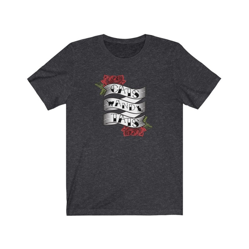 May include: A dark heather grey t-shirt featuring a white banner design that reads "Cats and Tats" with two red roses on either side of the banner.