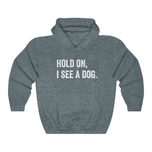 Pode incluir: Uma camisa de frio com capuz azul escuro com o texto "HOLD ON, I SEE A DOG." impresso em branco na frente.