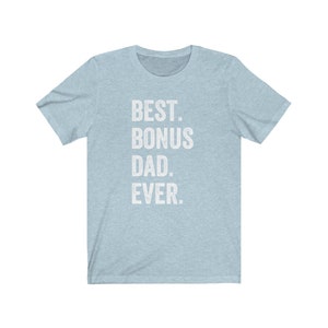 Puede incluir: Camiseta azul claro con el texto blanco "BEST. BONUS DAD. EVER." en letras de bloque. La camiseta tiene mangas cortas y cuello redondo. La tela parece ser un material suave y jaspeado.