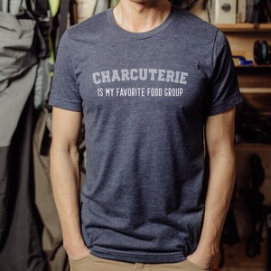 Peut inclure: Un t-shirt bleu fonc&eacute; avec le texte "CHARCUTERIE IS MY FAVORITE FOOD GROUP" en blanc.