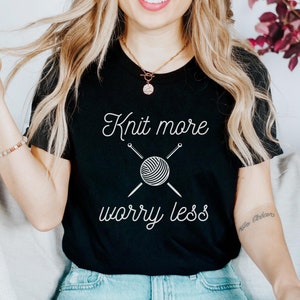 May include: A black t-shirt with the text "Knit more worry less" in white. The text is accompanied by a graphic of a ball of yarn with knitting needles.