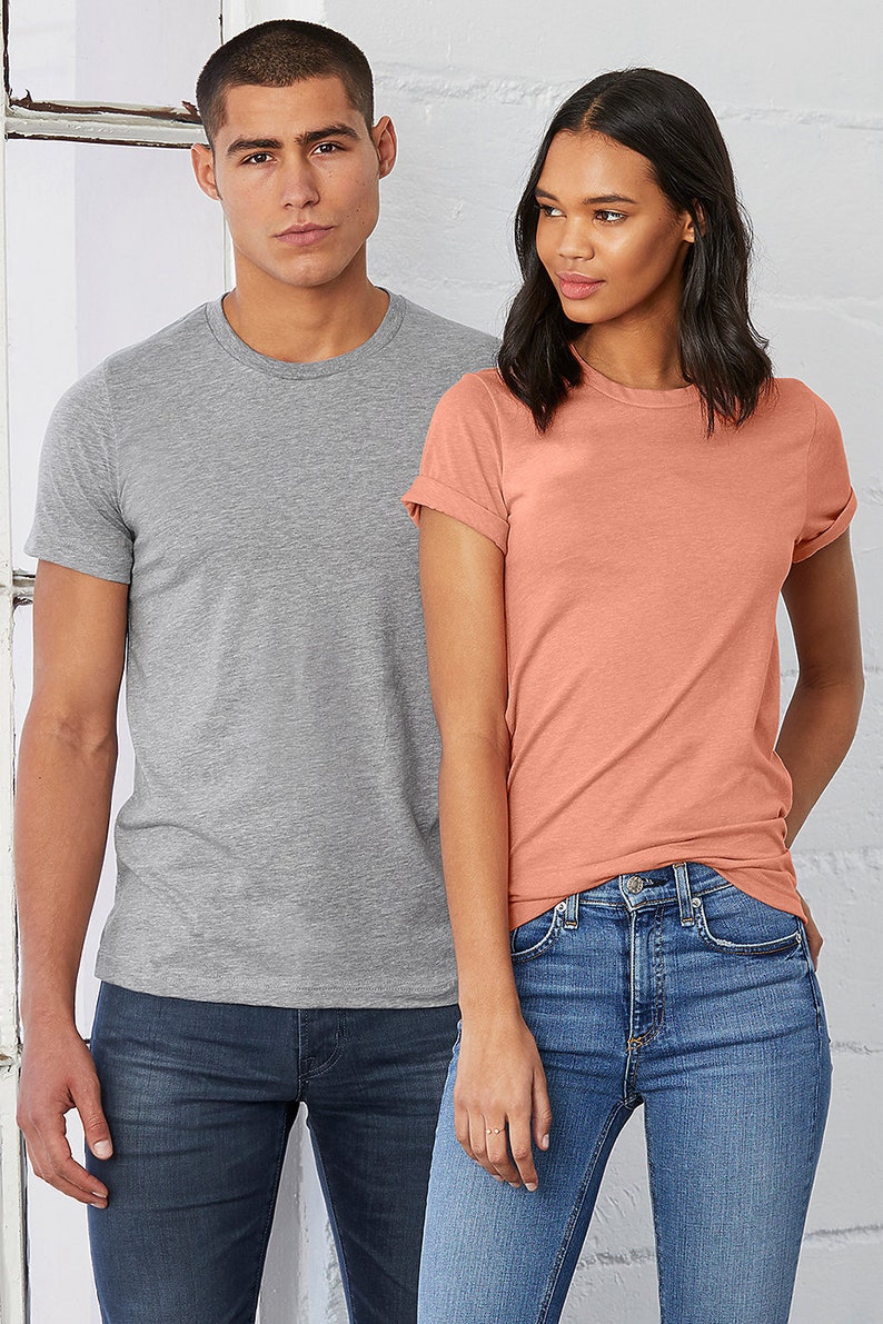 May include: Two people wearing short-sleeved t-shirts. The person on the left is wearing a heather grey t-shirt and the person on the right is wearing a coral t-shirt. Both people are wearing blue jeans.