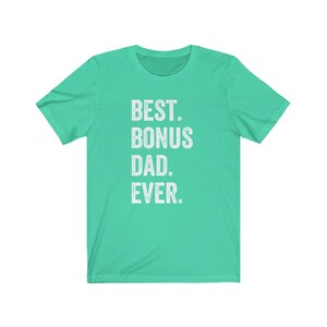 Puede incluir: Una camiseta de color turquesa con el texto "BEST. BONUS DAD. EVER." impreso en blanco. La camiseta tiene mangas cortas y cuello redondo. El texto est&aacute; centrado en la parte delantera de la camiseta.