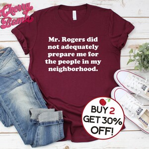 Puede incluir: Una camiseta color burdeos con texto blanco que dice "Mr. Rogers no me prepar&oacute; adecuadamente para la gente de mi vecindario." Un c&iacute;rculo rojo con una cereza blanca y el texto "COMPRA 2, LLEVA 30% DE DESCUENTO!" se encuentra en la esquina inferior derecha de la imagen.