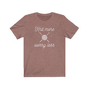 May include: A heather brown t-shirt with the text "Knit more worry less" in white. The text is accompanied by a graphic of a ball of yarn and two knitting needles.