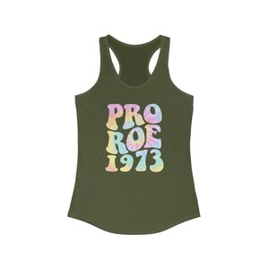 May include: Olive green racerback tank top with the words "PRO ROE 1973" in a tie-dye style font. The text is in pastel colors of pink, yellow, and blue. The tank top is made of a soft material.